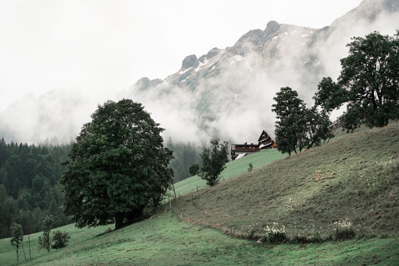 Serene mountain landscape with a chalet nestled among misty peaks and lush green terrain.