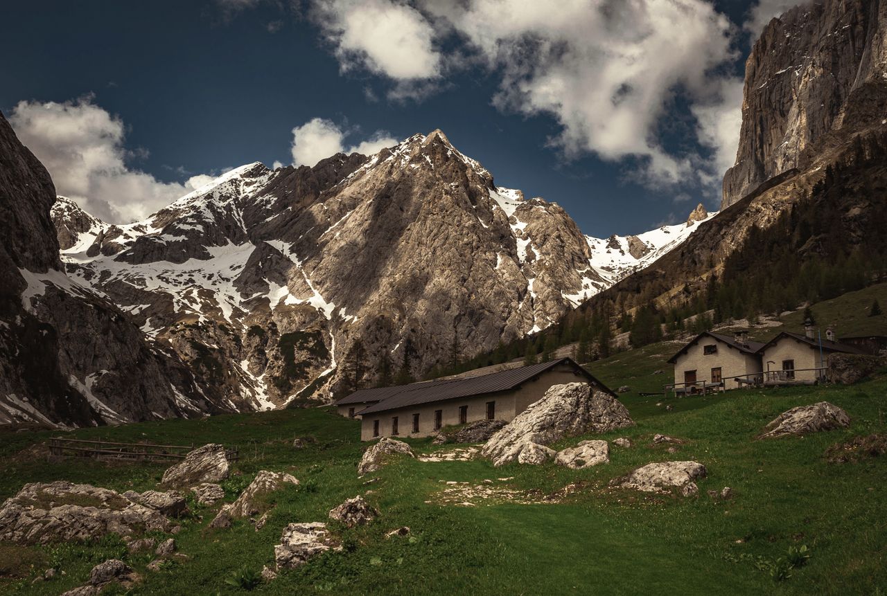 Charming alpine village nestled at the foot of towering mountains under a dramatic sky.